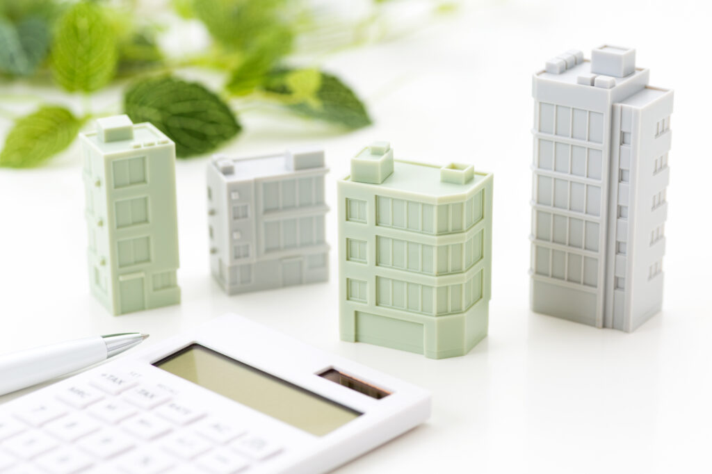 ホテルのミニチュアとペンと計算機のイメージ